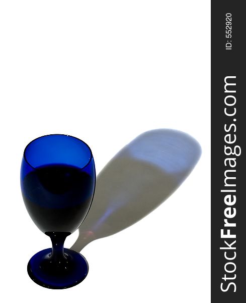 Cobalt blue glass filled with wine casts blue shadow on white background - copy space. Cobalt blue glass filled with wine casts blue shadow on white background - copy space