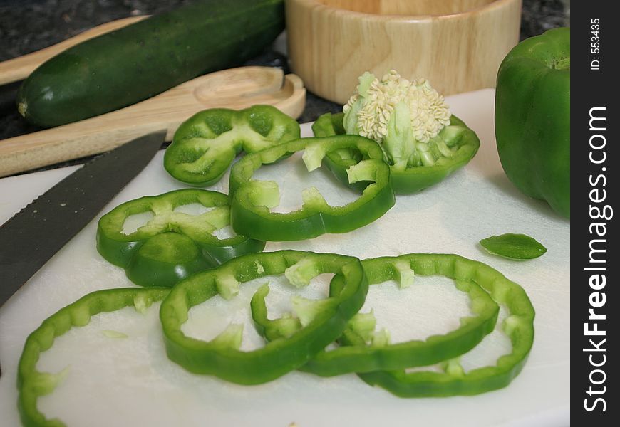 Green bell peppers on a cutting board, being cut into slices. Green bell peppers on a cutting board, being cut into slices