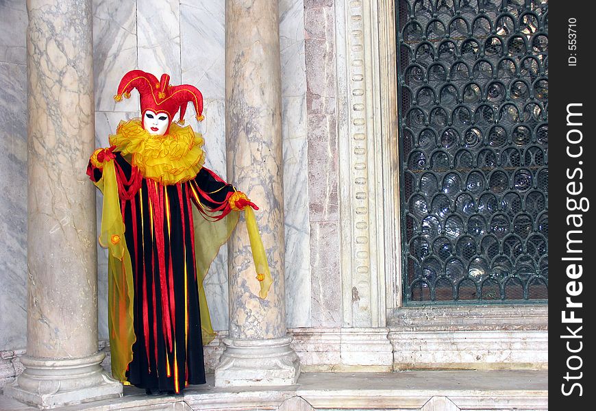Carnival of Venice, Italy: Person wearing beautiful mask and costume in the colors red, yellow and black between two pillars made of marble. [[ More Carnival photos ]]. Carnival of Venice, Italy: Person wearing beautiful mask and costume in the colors red, yellow and black between two pillars made of marble. [[ More Carnival photos ]]