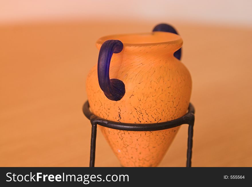 Greek vase close-up syle with blue and orange colors in a metal support on wood table