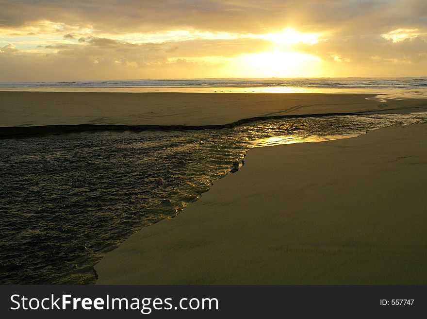 Texure and ripples on the top of a river of erosion running across a beach and into the ocean at sunset. Texure and ripples on the top of a river of erosion running across a beach and into the ocean at sunset.