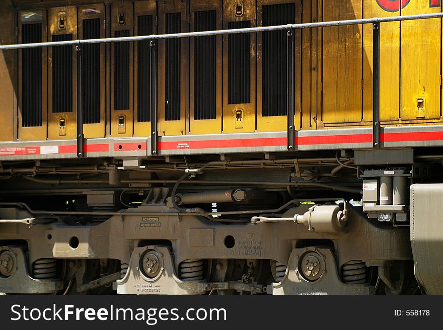Close or cropped view of a yellow train engine or locomotive, including suspension springs, engine vents, and guard railing. Close or cropped view of a yellow train engine or locomotive, including suspension springs, engine vents, and guard railing.