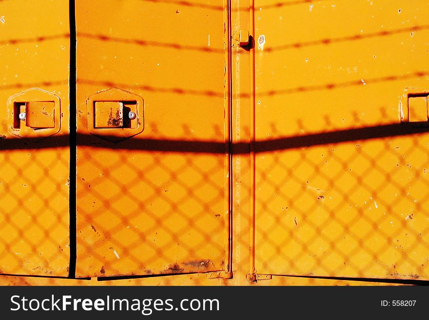 Yellow doors in an industrial stock yard showing silhouettes of barbed wire and chain link fence. Yellow doors in an industrial stock yard showing silhouettes of barbed wire and chain link fence.