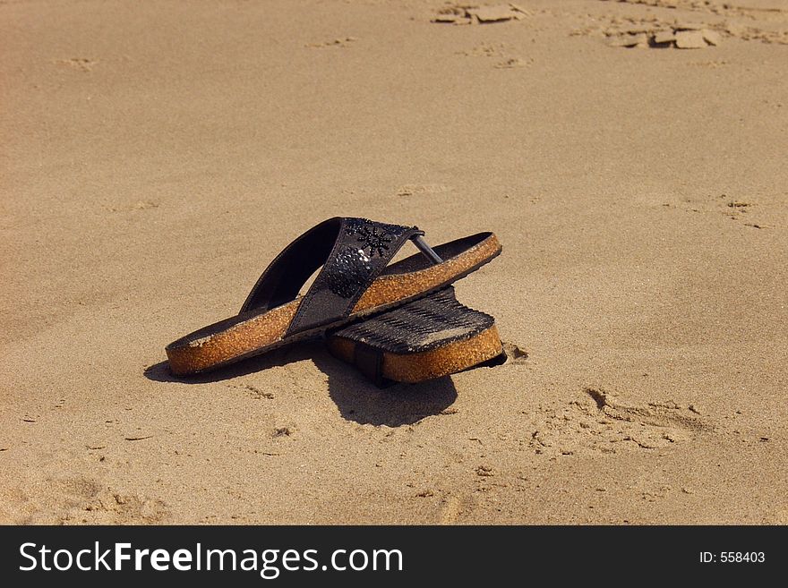 A pair of worn sandals laying on a sandy beach. A pair of worn sandals laying on a sandy beach.