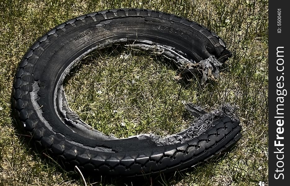 An old, worn, shredded tire left in the crab grass