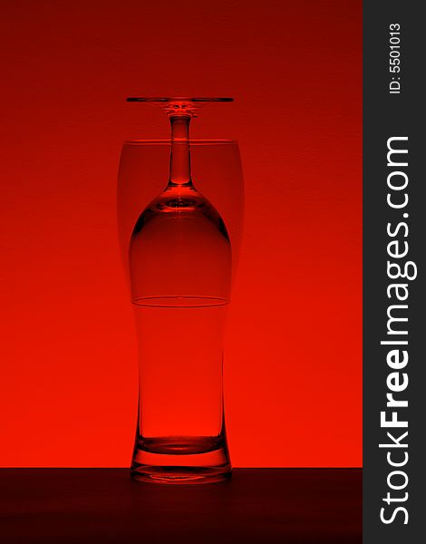 A wine and a beer glass put one into another to make optical effect. Red-toned for a dramatic look. A wine and a beer glass put one into another to make optical effect. Red-toned for a dramatic look.