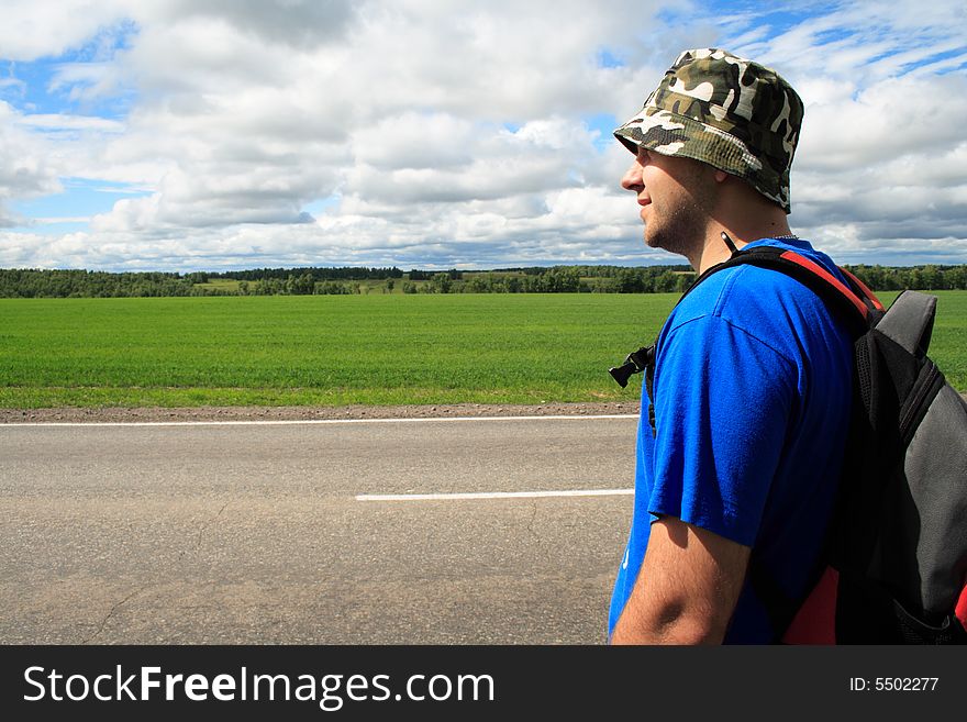 Man on a roadside of road on a background of clouds and the blue sky. Man on a roadside of road on a background of clouds and the blue sky