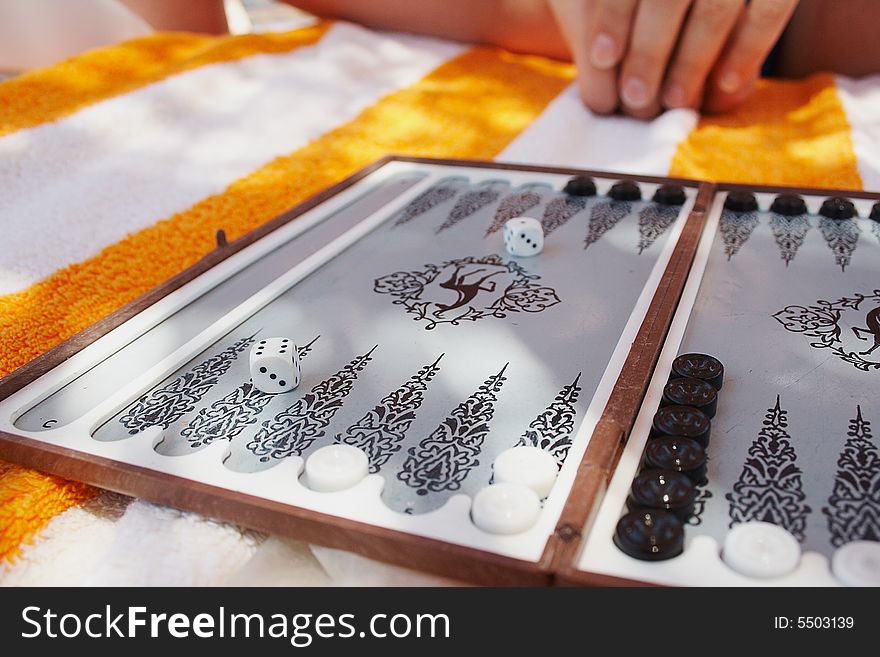 Open board of backgammon is laying on striped towel. Open board of backgammon is laying on striped towel