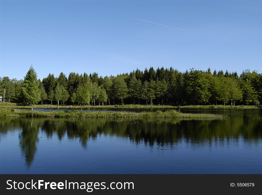 Picture of a calm sunny lake with reflecting in water from across the lake. Picture of a calm sunny lake with reflecting in water from across the lake