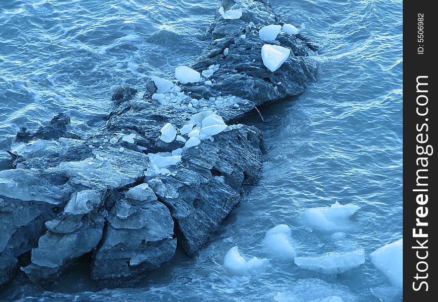 Glacier remnants floating past rock formation.