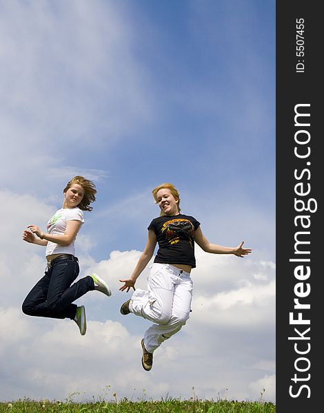 The two happy jumping girls on a background of the blue sky