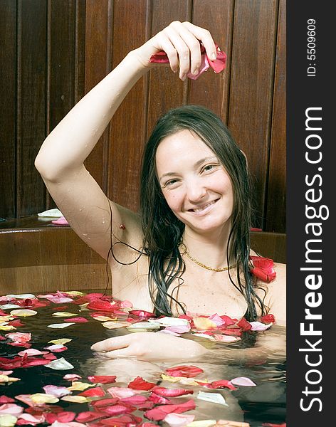 Woman smiling as she drops flower petals in a tub. Vertically framed photograph. Woman smiling as she drops flower petals in a tub. Vertically framed photograph.