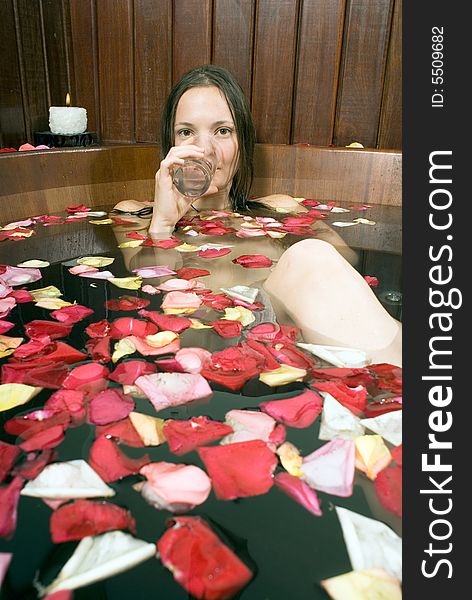 Woman sips water as she lounges in a spa tub filled with flower petals. Vertically framed photograph. Woman sips water as she lounges in a spa tub filled with flower petals. Vertically framed photograph.