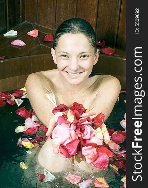 Attractive young women, covered in flower petals, soaking in a large dark-wood bathtub at spa and holding up her hands covered in petals. Vertically framed close-up shot. Attractive young women, covered in flower petals, soaking in a large dark-wood bathtub at spa and holding up her hands covered in petals. Vertically framed close-up shot.