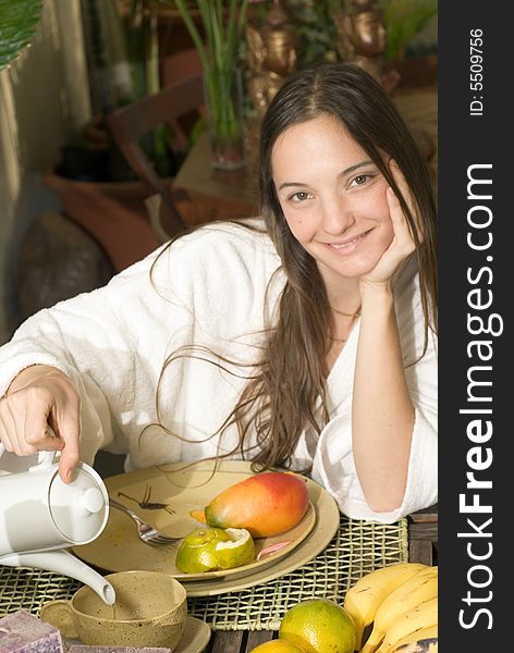 Woman smiles as she has breakfast. There is fruit on her plate and she is pouring tea. Vertically framed photograph. Woman smiles as she has breakfast. There is fruit on her plate and she is pouring tea. Vertically framed photograph.