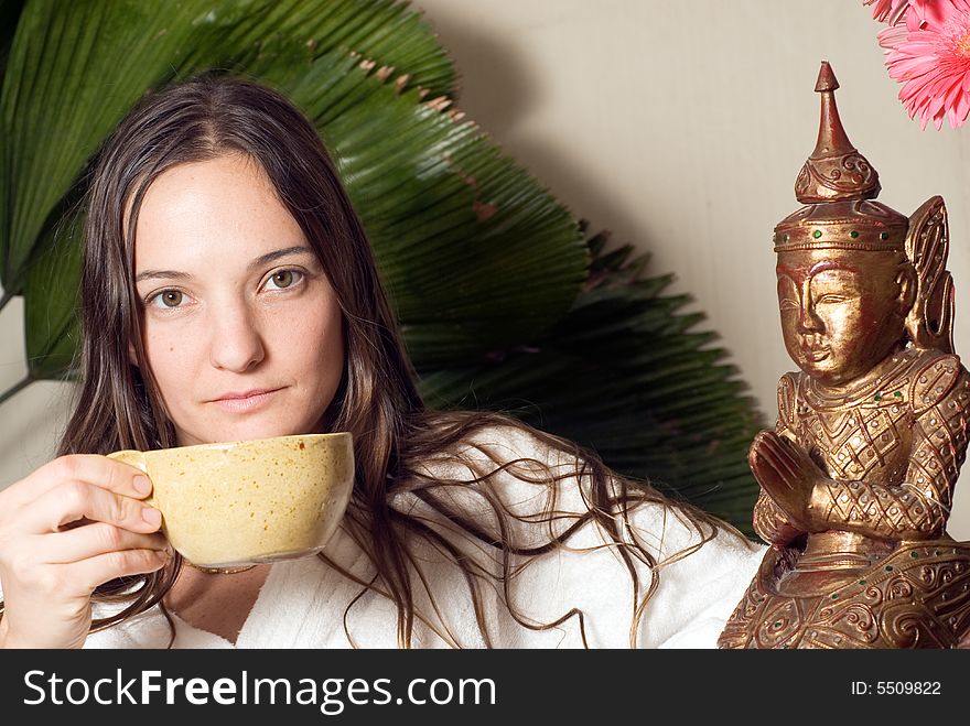 Woman holds a tea cup. She sits next to a bronze statue. Horizontally framed photograph. Woman holds a tea cup. She sits next to a bronze statue. Horizontally framed photograph.