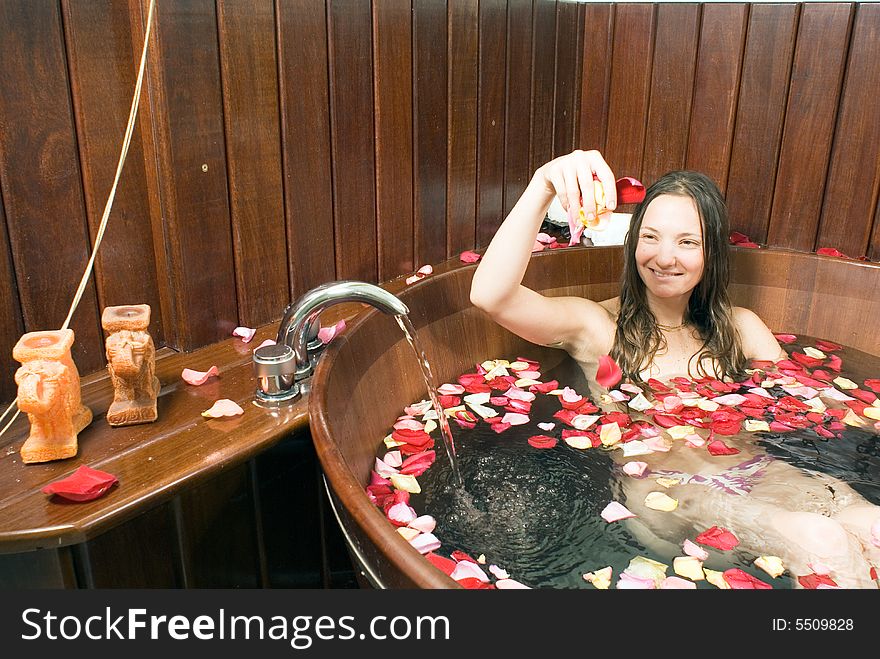 An attractive young girl sitting in a water full bathtub. Rose petals floating in bathtub while water is running. Horizontally framed shot. An attractive young girl sitting in a water full bathtub. Rose petals floating in bathtub while water is running. Horizontally framed shot.