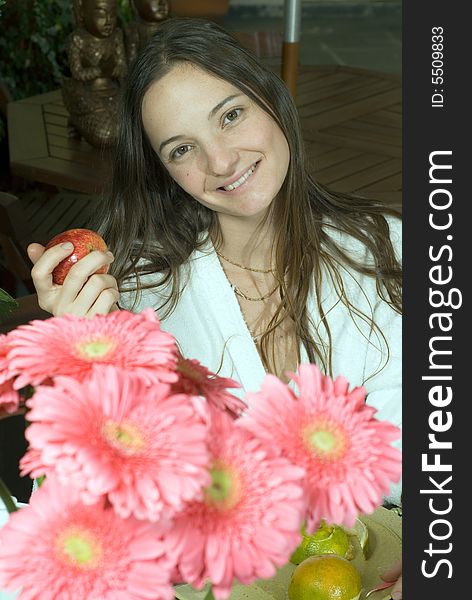 Woman smiles as she poses by pink flowers and holds an apple. Vertically framed photograph. Woman smiles as she poses by pink flowers and holds an apple. Vertically framed photograph.