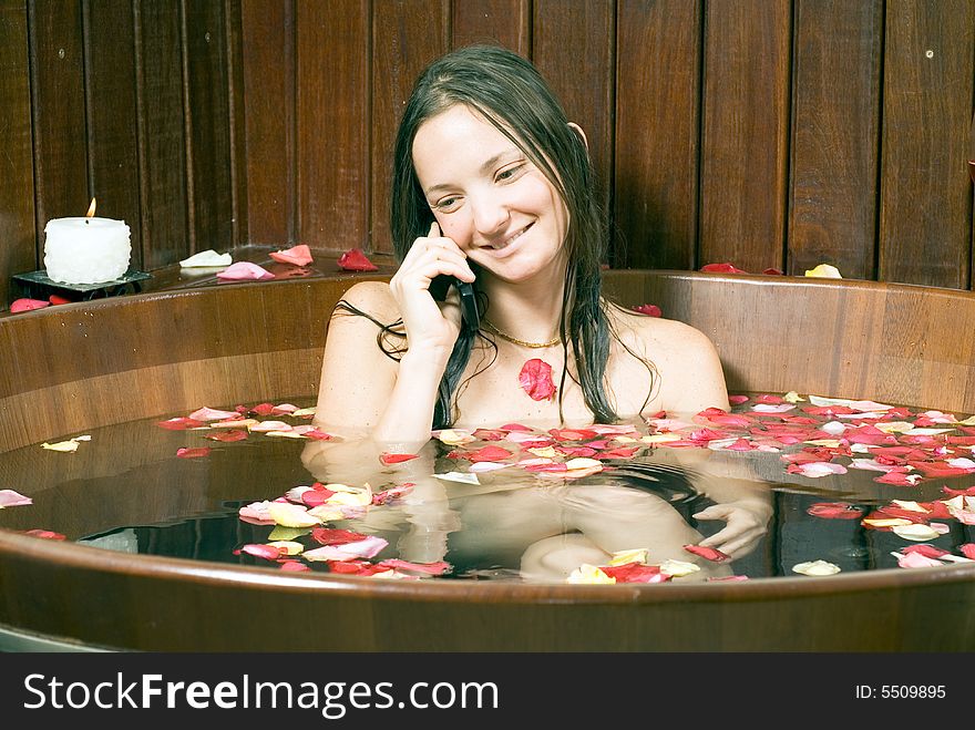 An adorable young lady happily talking on the phone, while in a rose filled bathtub. Horizontally framed shot. An adorable young lady happily talking on the phone, while in a rose filled bathtub. Horizontally framed shot.