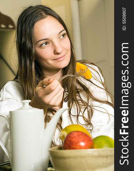 Woman smiles as she has breakfast. There is fruit and tea on the table. Vertically framed photograph. Woman smiles as she has breakfast. There is fruit and tea on the table. Vertically framed photograph.