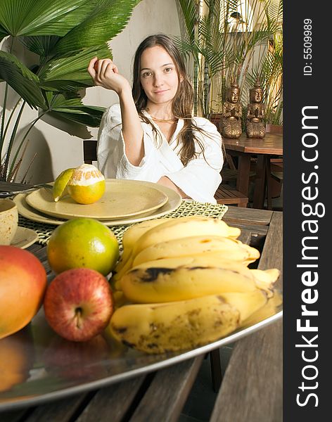 Woman smiles as she has breakfast. There are many fruits on the table. Vertically framed photograph. Woman smiles as she has breakfast. There are many fruits on the table. Vertically framed photograph.