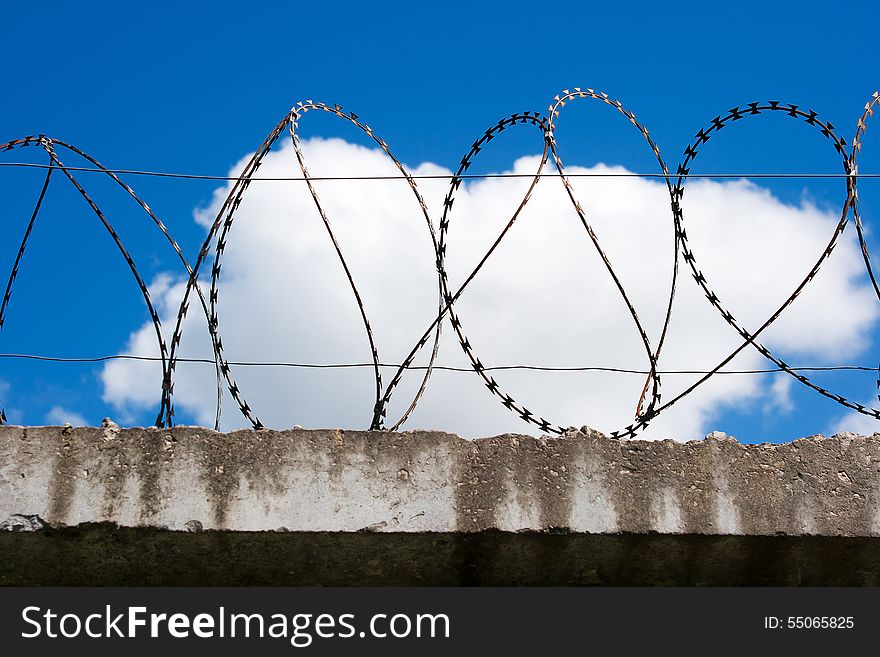 Barbed wire on top of the concrete fence with blue sky with clouds closeup. Barbed wire on top of the concrete fence with blue sky with clouds closeup