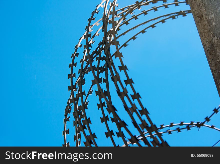Coil of barbed wire on a concrete fence with blue sky closeup