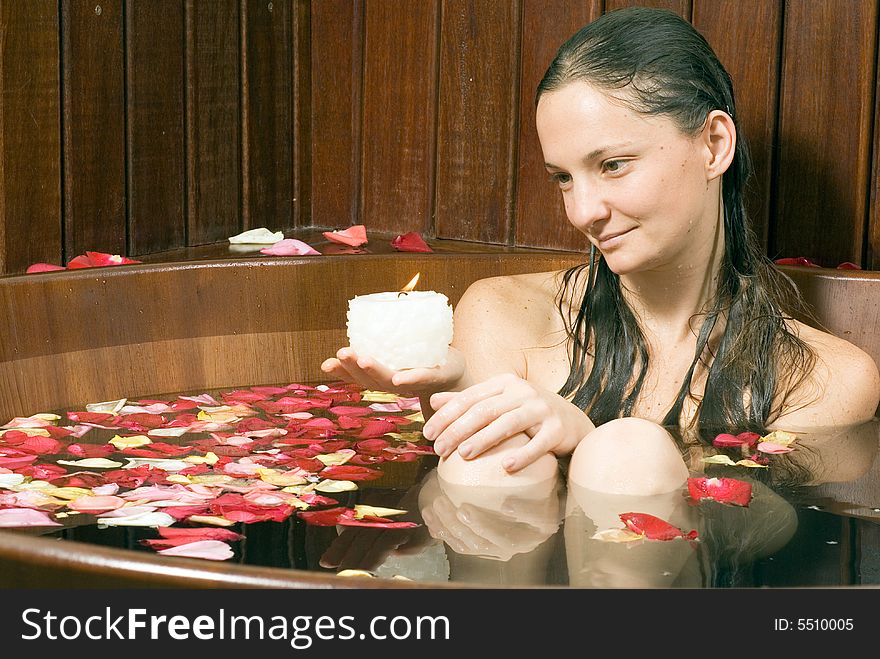 Woman smiles she looks at a candle. She is relaxing in a spa tub filled with flowers. Horizontally framed photograph. Woman smiles she looks at a candle. She is relaxing in a spa tub filled with flowers. Horizontally framed photograph.