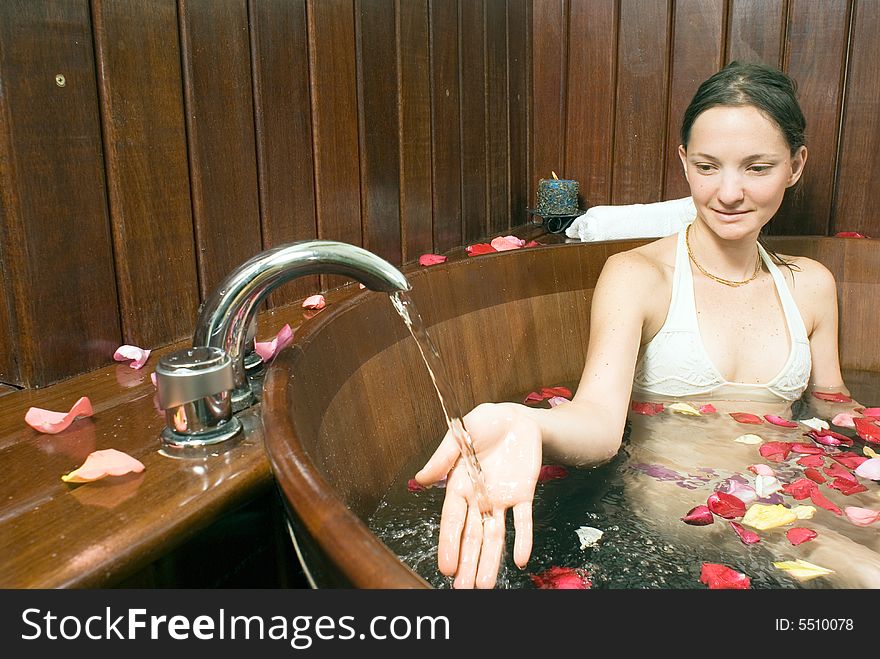 Woman relaxes in a spa tub filled with flowers and holds her hand under a faucet. Horizontally framed photograph. Woman relaxes in a spa tub filled with flowers and holds her hand under a faucet. Horizontally framed photograph