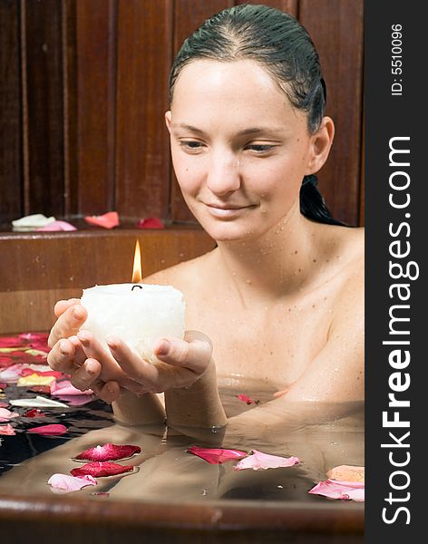 Woman smiles she looks at a candle. She is relaxing in a spa tub filled with flowers. Vertically framed photograph. Woman smiles she looks at a candle. She is relaxing in a spa tub filled with flowers. Vertically framed photograph.