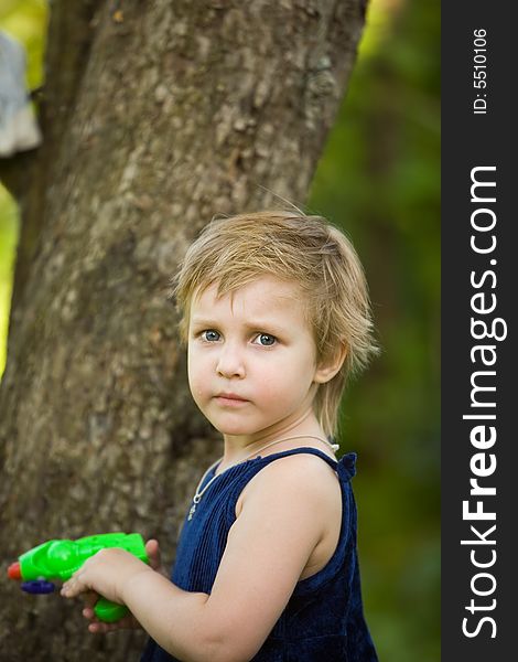 The little girl in a dark blue dress is going to shoot from a water pistol in summer day. The little girl in a dark blue dress is going to shoot from a water pistol in summer day