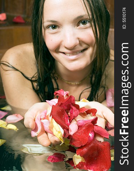 Woman smiles as she scoops up flower petals in her hands while she bathes. Vertically framed photograph. Woman smiles as she scoops up flower petals in her hands while she bathes. Vertically framed photograph.
