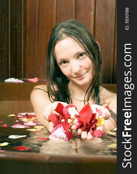 An attractive young lady holding multi-colored rose petals while sitting in a bathtub full of water. Vertically framed shot. An attractive young lady holding multi-colored rose petals while sitting in a bathtub full of water. Vertically framed shot.