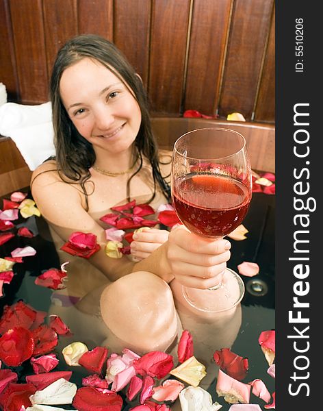 An attractive young lady, holding a drink. She is sitting in a bathtub full of various rose petals. Vertically framed shot. An attractive young lady, holding a drink. She is sitting in a bathtub full of various rose petals. Vertically framed shot.