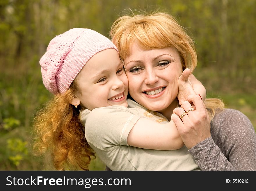 The beautiful little girl in a pink cap embraces mum with light hair. The beautiful little girl in a pink cap embraces mum with light hair