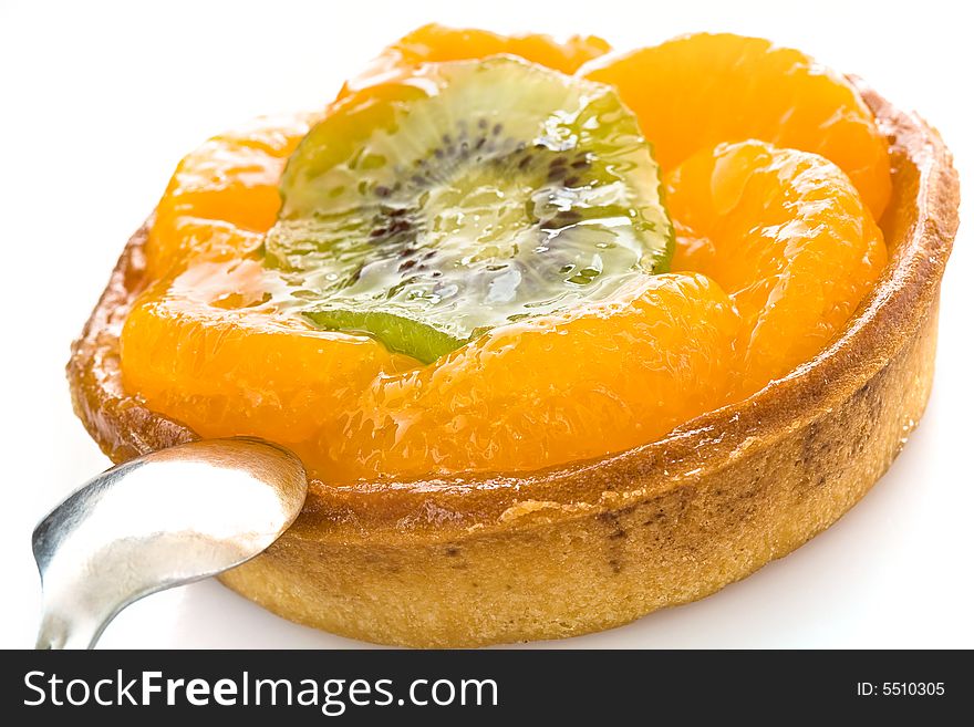 Round cake with segments of a tangerine and a circle of kiwi close up on a white background with a spoon. Round cake with segments of a tangerine and a circle of kiwi close up on a white background with a spoon