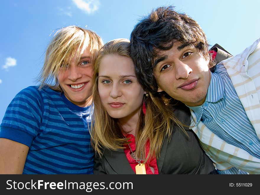 Three young friends embrace over sky background