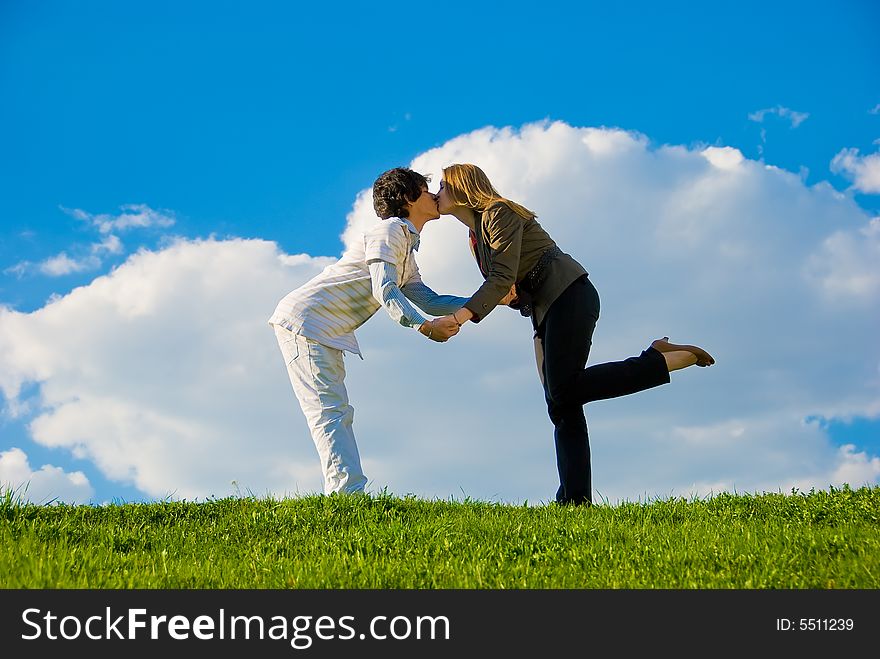 Young couple kissing on the lawn over sky background. Young couple kissing on the lawn over sky background
