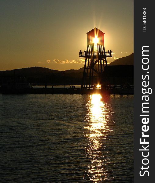 Observation tower in silhouette at sunset on Memphremagog lake in Magog, province of Quebec, Canada, with Mont-Orford in background. Observation tower in silhouette at sunset on Memphremagog lake in Magog, province of Quebec, Canada, with Mont-Orford in background