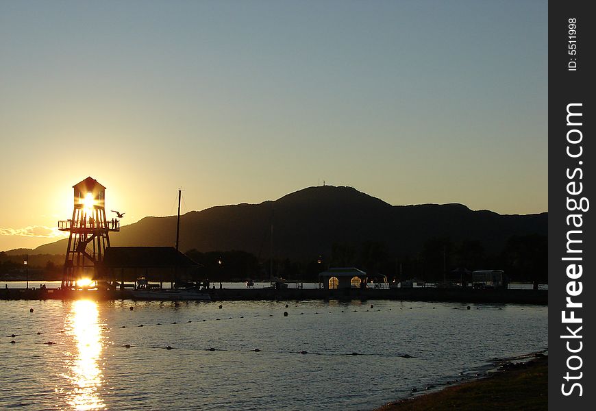 Observation tower in silhouette at sunset on Memphremagog lake, province of Quebec, Canada, with Mont-Orford in background. Observation tower in silhouette at sunset on Memphremagog lake, province of Quebec, Canada, with Mont-Orford in background