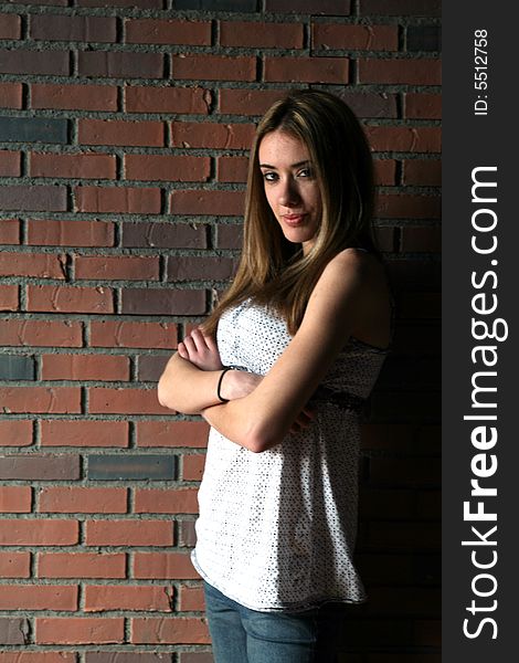 Natural light portrait of a teenage girl with her arms crossed in front of a brick wall.