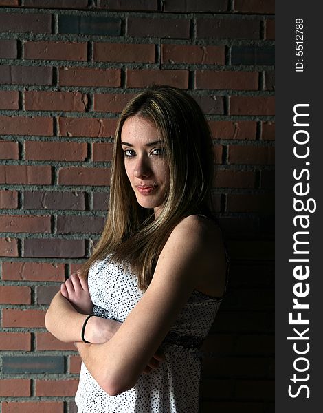 Pretty teenage girl with arms crossed; against a brick wall