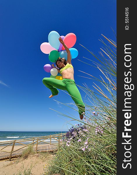 Girl with colorful balloons jumping on the beach