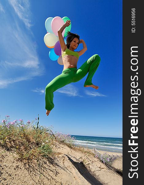 Girl with colorful balloons jumping on the beach