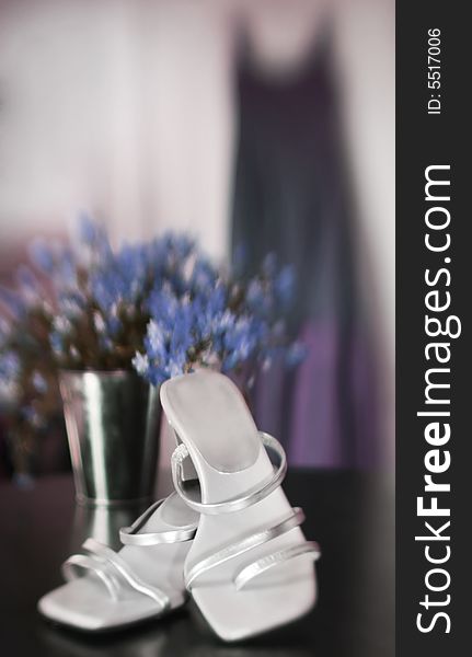 A bridesmaids dress hangs in the background with shoes in the foreground. A bridesmaids dress hangs in the background with shoes in the foreground