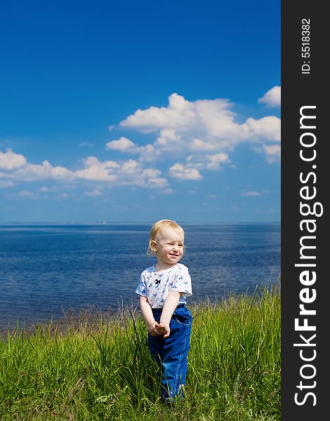 Small girl in green grass over the blue sky near the river. Small girl in green grass over the blue sky near the river