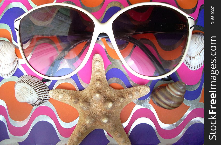 Solar glasses and different seashells on a shining and bright background