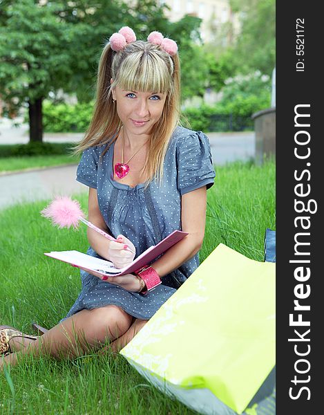 Beauty shopping blonde girl on green grass with paper bag