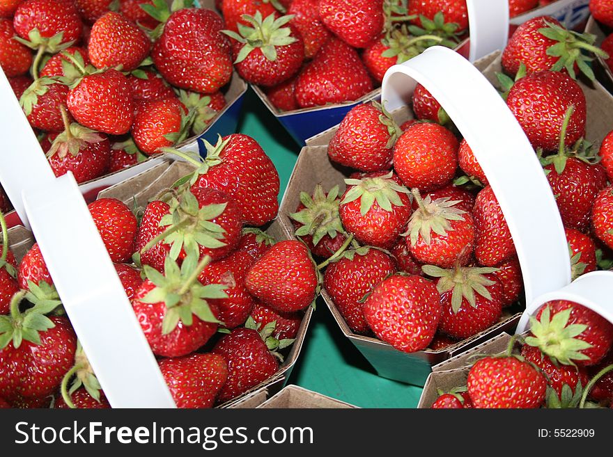 Strawberries are for sale in baskets in a market stall. Strawberries are for sale in baskets in a market stall