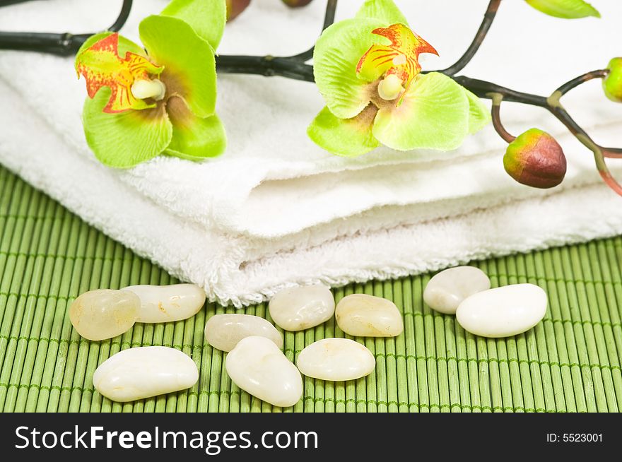 Smooth bright pebbles and towel with artificiell orchids on green bamboo. Smooth bright pebbles and towel with artificiell orchids on green bamboo